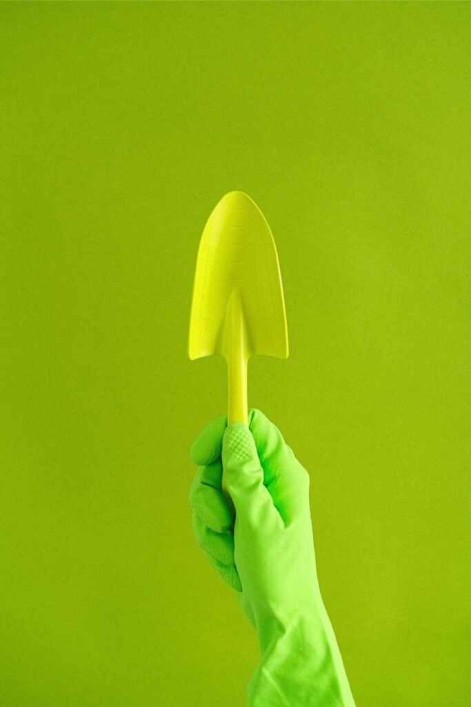a hand wearing a green gloves holding a green shovel